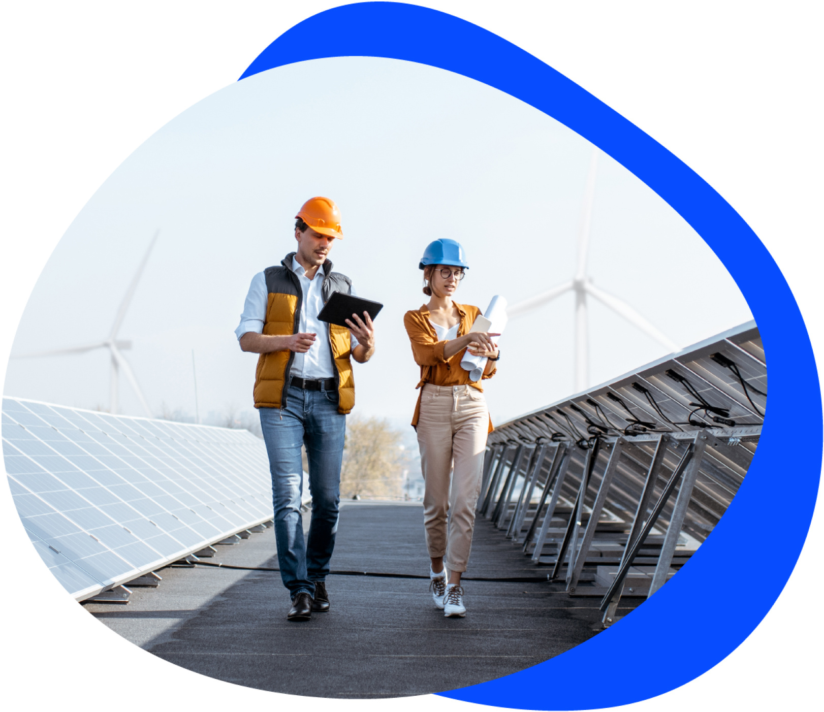 a man and woman with hard hats on walking between solar panels outside