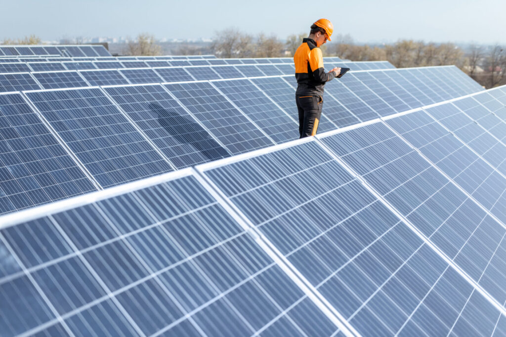 Engineer in protective workwear walking and examining photovoltaic panels.